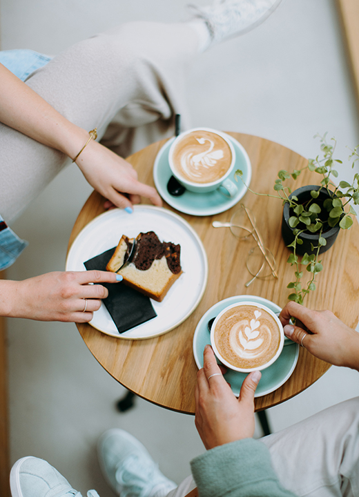 People seated at small cafe table with food and lattes with decorative foam.